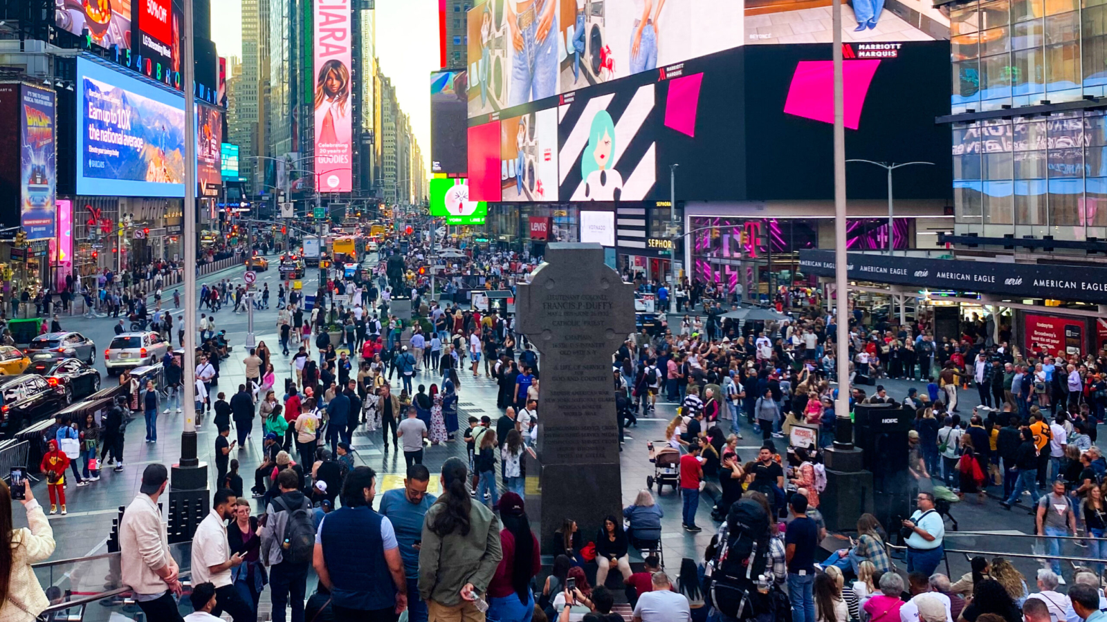 Image of Times Square taken on October 3rd, 2024, on top of the “Red Stairs” displaying the billboard lights, thousands of visitors, and dance performance gathered in a circle on the left.